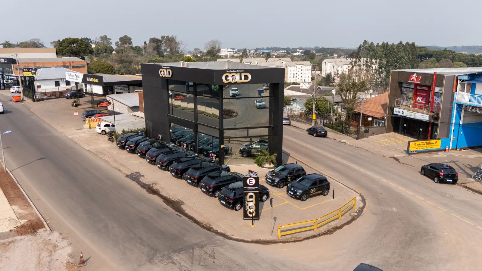 Vista aérea da matriz da Gold Merchandising em Passo Fundo: prédio preto com letreiro dourado e a frota de carros identificados estacionada na frente